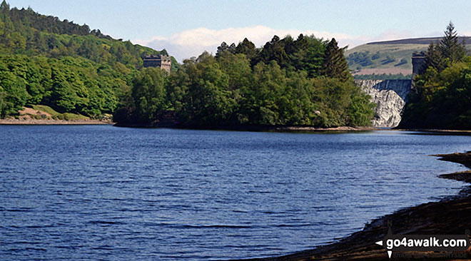 Island Plantation in the middle of Derwent Reservoir with water cascading over Howden Reservoir Dam beyond