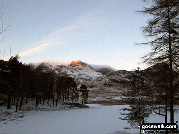 The last rays on sunshine on The Langdale Pikes across a frozen Blea Tarn (Langdale)