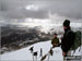 Friends on the summit of Yr Aran in the snow with Beddgelert below (left centre) and Moel Hebog on the horizon (right)